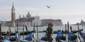 Eine Frau mit seinem Selfiestick steht in Venedig am Wasser, hinter ihr Boote