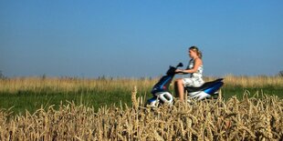 Eine Frau fährt auf einem Elektroroller über eine Landstrasse