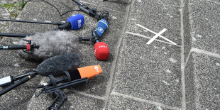 Mikrofone verschiedener Sender liegen auf dem Asphalt, alle ausgerichtet auf den selben Punkt