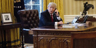 Ein Mann sitzt an einem großen Schreibtisch und telefoniert