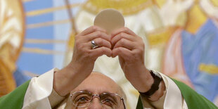 Alter Mann mit Brille hebt eine Oblate hoch