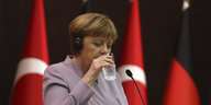 Angela Merkel hebt ein Glas Wasser zum Mund, hinter ihr die Fahnen der Türkei und Deutschlands
