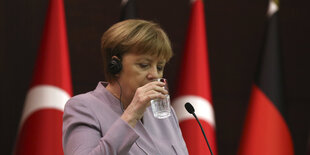 Angela Merkel hebt ein Glas Wasser zum Mund, hinter ihr die Fahnen der Türkei und Deutschlands