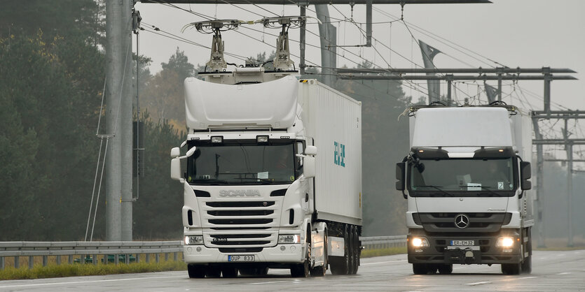 Zwei LKW fahren auf einer Autobahn über der Stromleitungen hängen