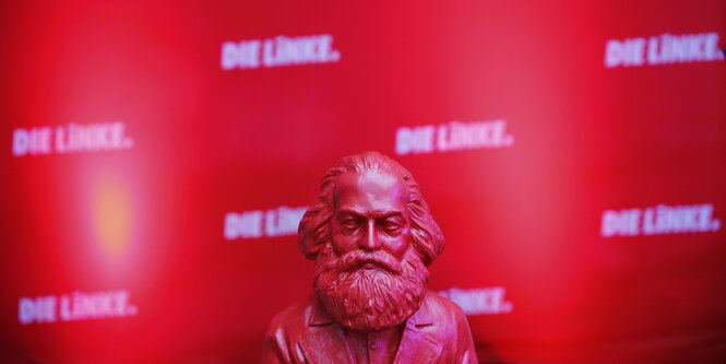 Eine rote Büste von Karl Marx steht vor einem roten Hintergrund, auf dem mehrfach in weiß „Die Linke“ steht