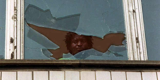 Ein Mann schaut aus dem eingeschlagegen Fenster des Heims Hoyerswerda