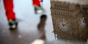 Rote Hosenbeine steigen über eine Pfütze, in der sich Westminster Palace spiegelt
