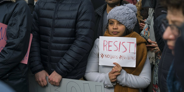 Eine Frau mit Mütze hält ein Schild hoch, auf dem "Resist" steht
