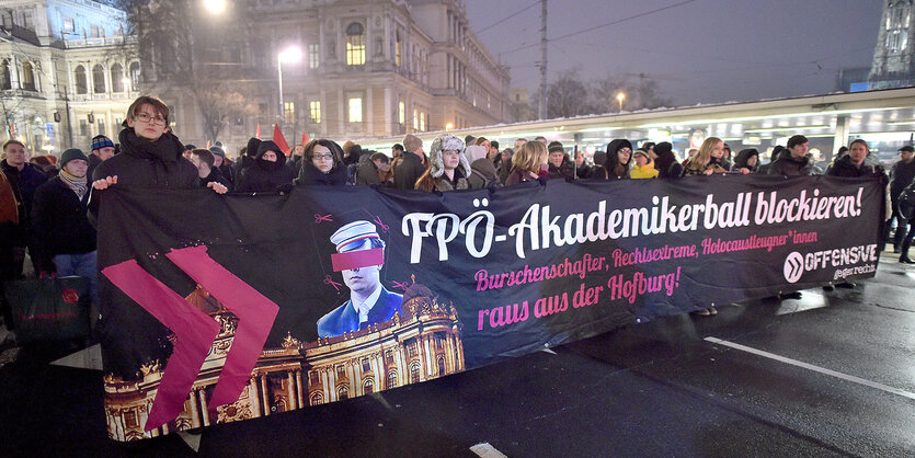 Mehrere Personen schreiten, ein Transparent haltend, einer Demonstration voran. Es ist Abend.