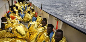 Gerettete Flüchtlinge sitzen in goldene Wärmedecken gehüllt auf einem Boot