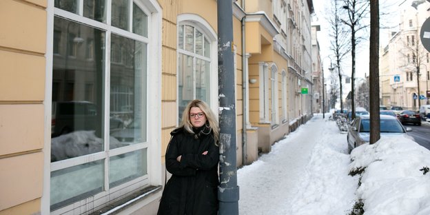 Susanne Schaper steht an eine Laterne angelehnt auf dem zugeschneiten Bürgersteig einer Straße
