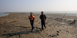 Zwei bewaffnete Männer laufen auf einer Sandbank