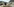 Ein Esel steht in einem Gebirge herum. Im Hintergrund Gebäude