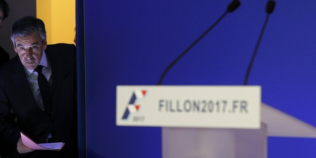 Ein leeres Rednerpult. Im Hintergrund schaut François Fillon durch die Kulissen hindurch