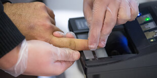 Zwei Hände in in Einweg-Handschuhen entnehmen einer anderen Hand einen Fingerabdruck