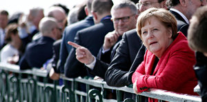 Angela Merkel lehnt gegen einen Zaun und ist von anderen Menschen umringt