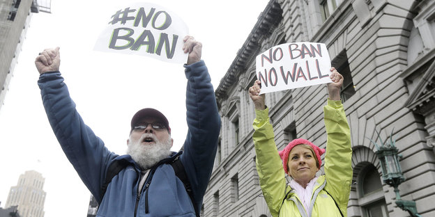 Zwei Menschen halten Plakate in die Höhe, auf denen "No ban, no wall" steht