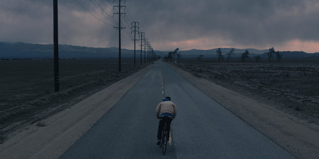 ein Junge fährt mit dem Rad auf der Mitte eines Highways, am Himmel dräuen schwere Wolken