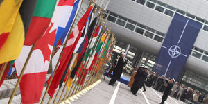 Eine Reihe Nationalfahnen weht vor dem Gebäude des Nato-Hauptquartierts, daneben exerzieren Soldaten vor einer Nato-Fahne
