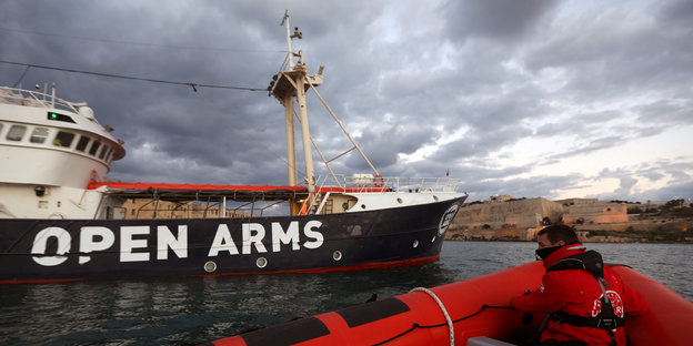 Auf einem Schiffsrumpf steht „Open Arms“, dafür liegt ein rotes Rettungsboot