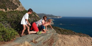 Kinder und eine Frau schauen an einer Steilküste herunter