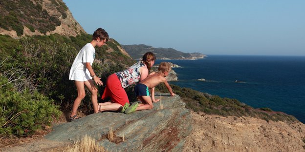 Kinder und eine Frau schauen an einer Steilküste herunter