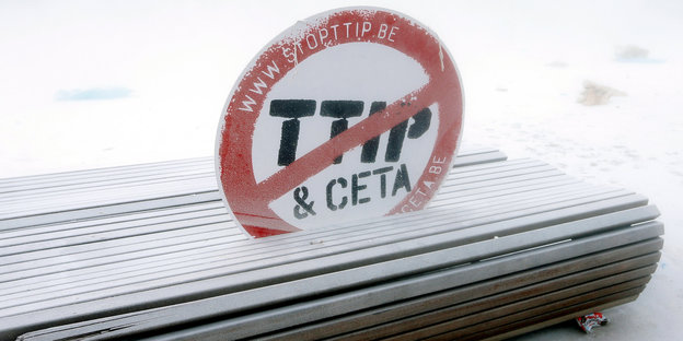Ein Schild mit dem durschgestrichenen Schriftzug "TTIP & Ceta" steckt in einer verschneiten Sitzbank