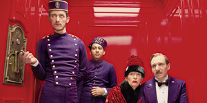 Der Liftboy und die Hotelgäste vor rotem Hintergrund in einer Szene von "The Grand Budapest Hotel"
