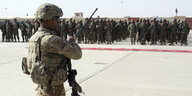 Ein US-Soldat in Kampfausrüstung und mit Maschinengewehr vor einer Truppe anderer Soldaten