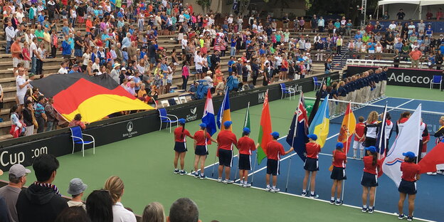 Menschen mit den Fahnen verschiedener Nationen in einem Tennisstadion, links im Bild: eine große Deutschlandfahne