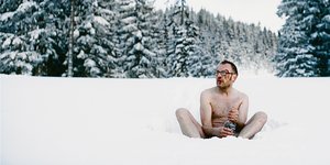 ein Mann sitzt nackt und blutend mit einer Flasche Schnaps auf einer verschneiten Fläche im Wald