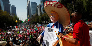 Eine Figur des US-Präsidenten Trump mit Sombrero und Hitler-Schild vor einer Menge Demonstranten