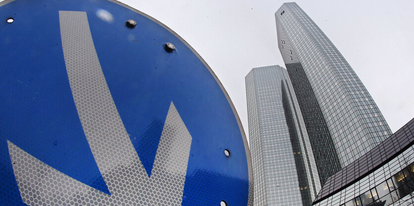 Der Pfeil eines Straßenschilds zeigt steil nach unten, im Hintergrund das Hauptquartier der Deutschen Bank