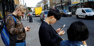 Junge Menschen am Straßenrand starren auf ihre Handys