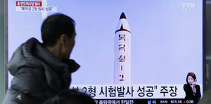 Ein Mann im Parka blickt auf einen Bildschirm, über den gerade der Raketentest Nordkoreas flackert