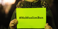 Frau hält gelbes Schild hoch mit Hashtag #NoMuslimBan