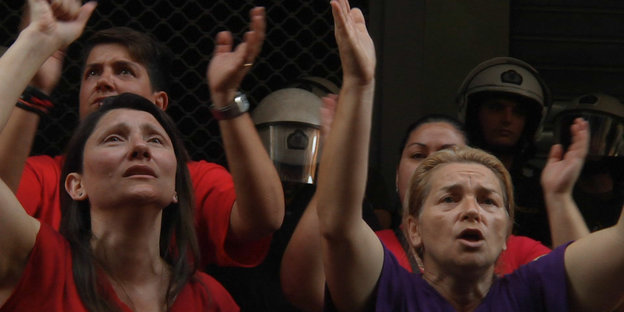 Frauen, die Hände protestierend erhoben, hinter ihnen behelmte Polizisten.