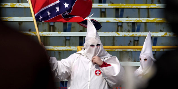 Zwei Menschen mit weißen Kutten und der Flagge der Konföderation