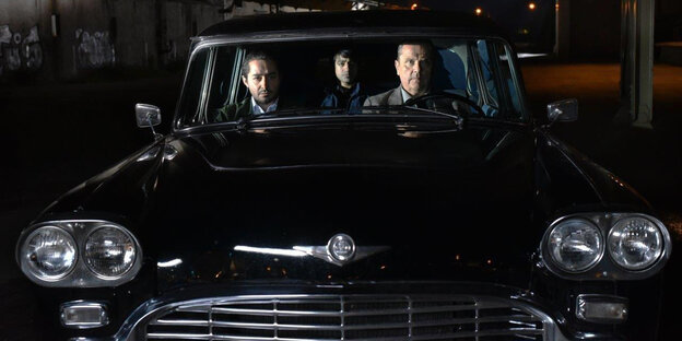 Drei Männer sitzen nachts in einem schwarzen Auto