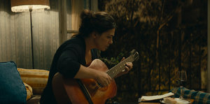 Die Schauspielerin Ia Shugliashvili sitzt in sich gekehrt am Fenster und spielt Gitarre