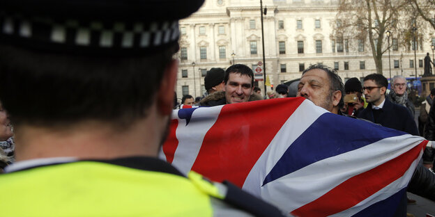 Ein Polizist steht vor Demonstranten mit einer britischen Fahne
