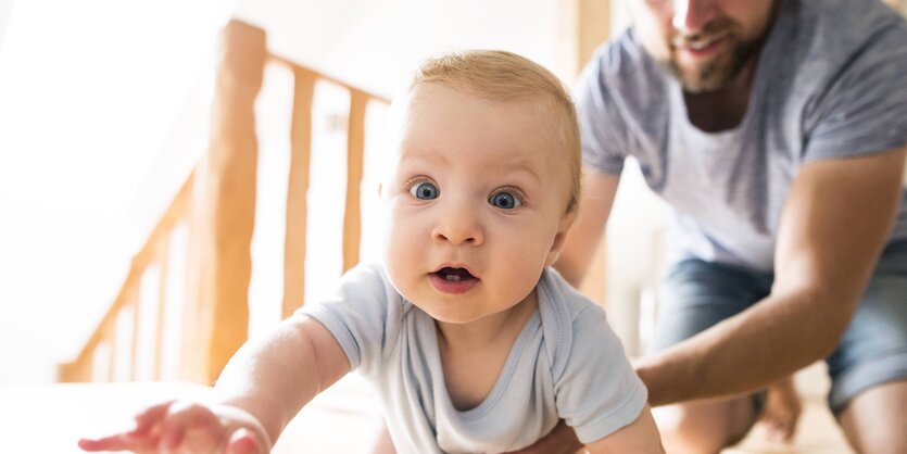 Krabbelndes Baby mit Vater im Hintergrund