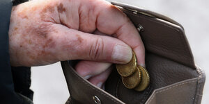 Eine fleckige Hand lässt Münzen in einen graubraunen Geldbeutel fallen