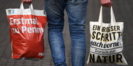 Ein Mann trägt eine Einweg-Plastiktüte des Discounters Penny und eine Mehrweg-Tasche des gleichen Unternehmens