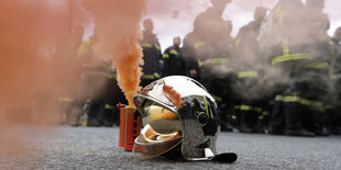 Roter Rauch steigt neben einem Feuerwehrhelm, der auf der Straße liegt, auf