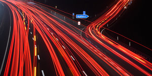 Langzeitbelichtung zeigt rote Leuchtspuren von PKW und LKW auf einer Autobahn