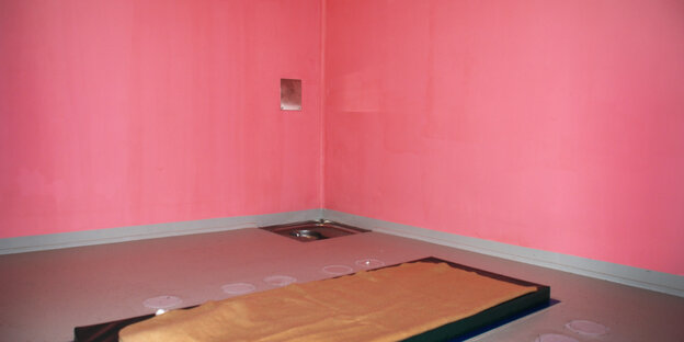 Eine pink gestrichene Gefängniszelle. Auf dem Boden liegt eine Matraze
