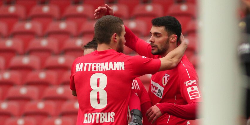 Fußballspieler des Energie Cottbus stehen auf dem Platz. Die Zuschauersitze sind leer