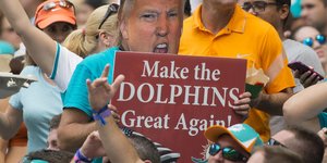 Ein Mann in zwischen Fans hält ein Schild hoch, auf dem Trump zu sehen ist. Darunter der Satz: „Make Dolphins great again"