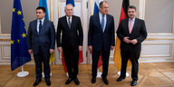 Vier Männer in Anzügen stehen nebeneinander, im Hintergrund verschiedene Nationalflaggen